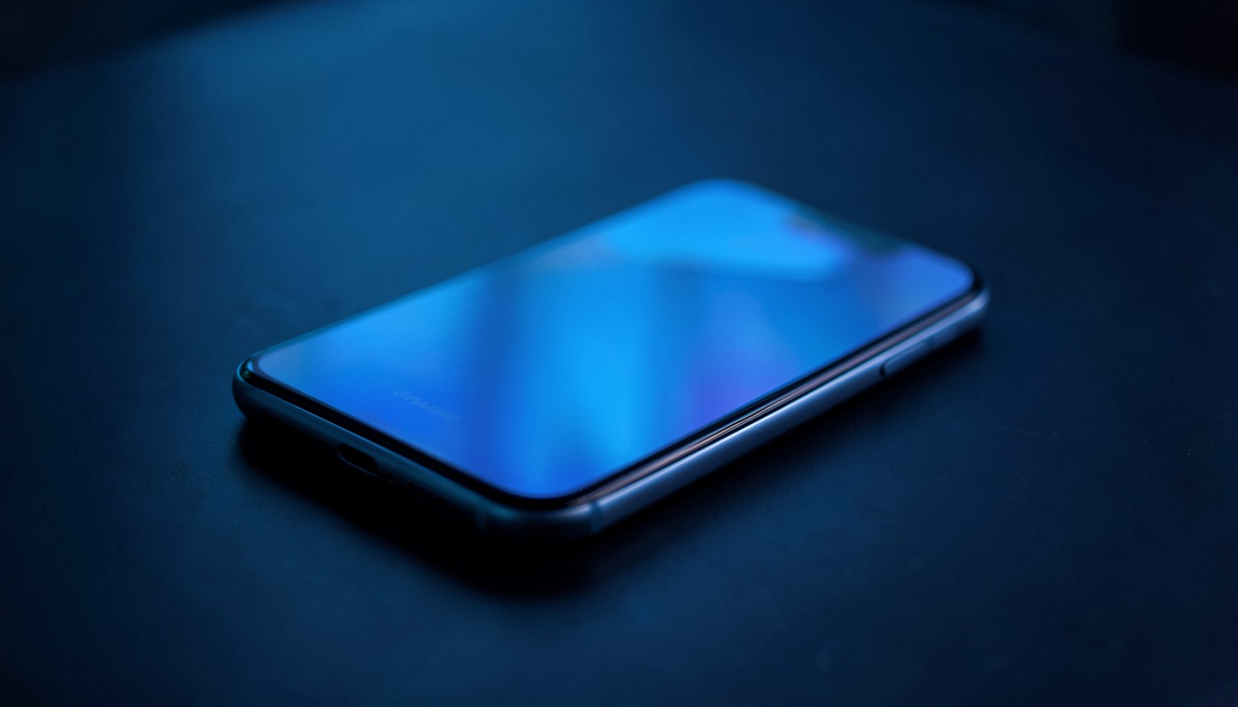 A sleek smartphone resting on a dark surface with soft blue ambient lighting, conveying a modern tech atmosphere