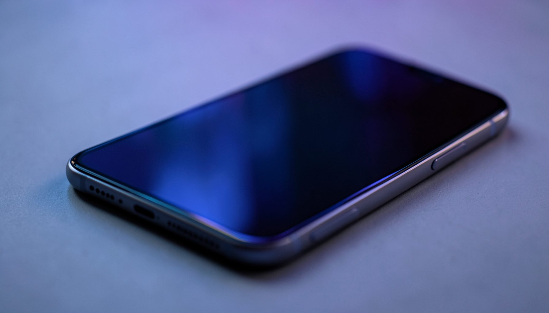 Dark smartphone screen with soft blue and purple ambient reflections on a matte surface