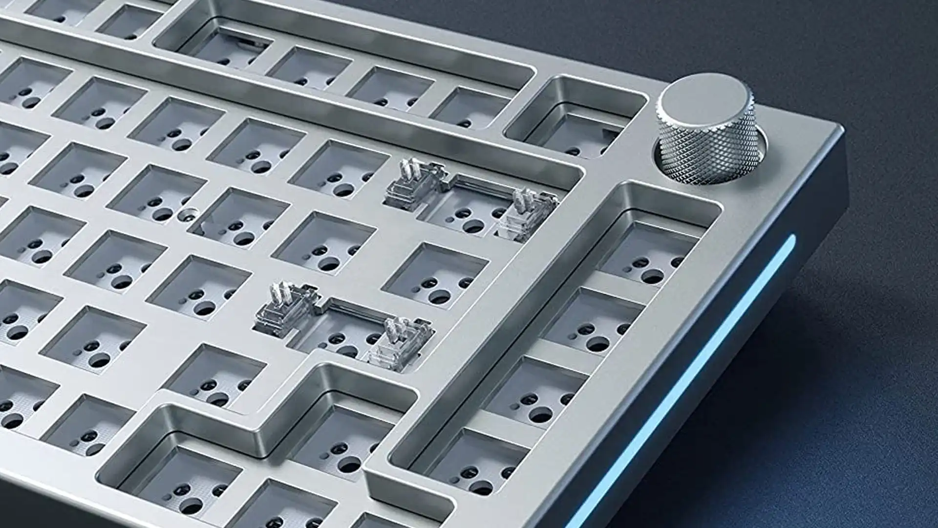 Close-up of a silver metal keyboard plate with switch sockets and two installed clear switches, with blue edge lighting